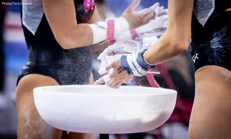 Two gymnasts chalk up during bars warmup